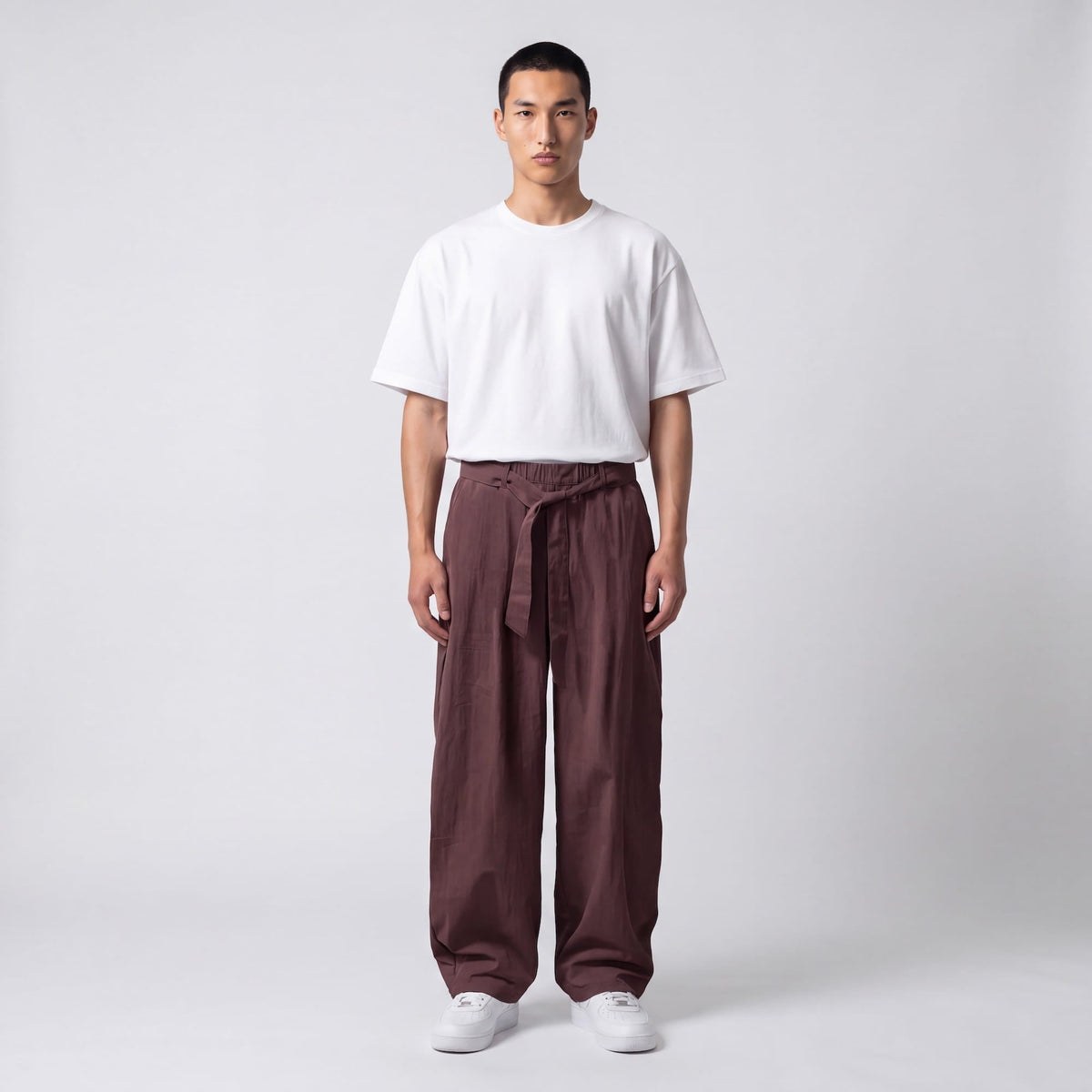 Full-length front view of a model in plum-brown wide-leg trousers with the waist belt tied, worn with a white tee. 7