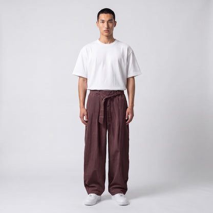 Full-length front view of a model in plum-brown wide-leg trousers with the waist belt tied, worn with a white tee. 7