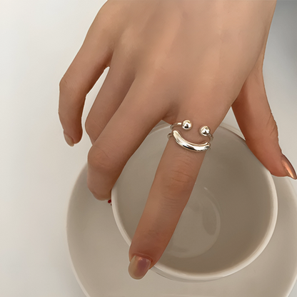 Smile-shaped silver ring on a model's index finger, hand resting over the rim of a white cup. 2