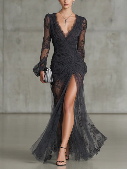 Model in a black floor-length lace dress with sheer sleeves, plunging V-neckline and high leg split, seen from the front, holding a clutch. 1