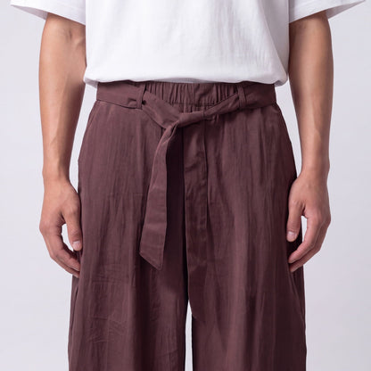 Close-up of the plum-brown trouser waistband, showing the elasticated back, stitched belt loops and a knotted fabric belt. 9