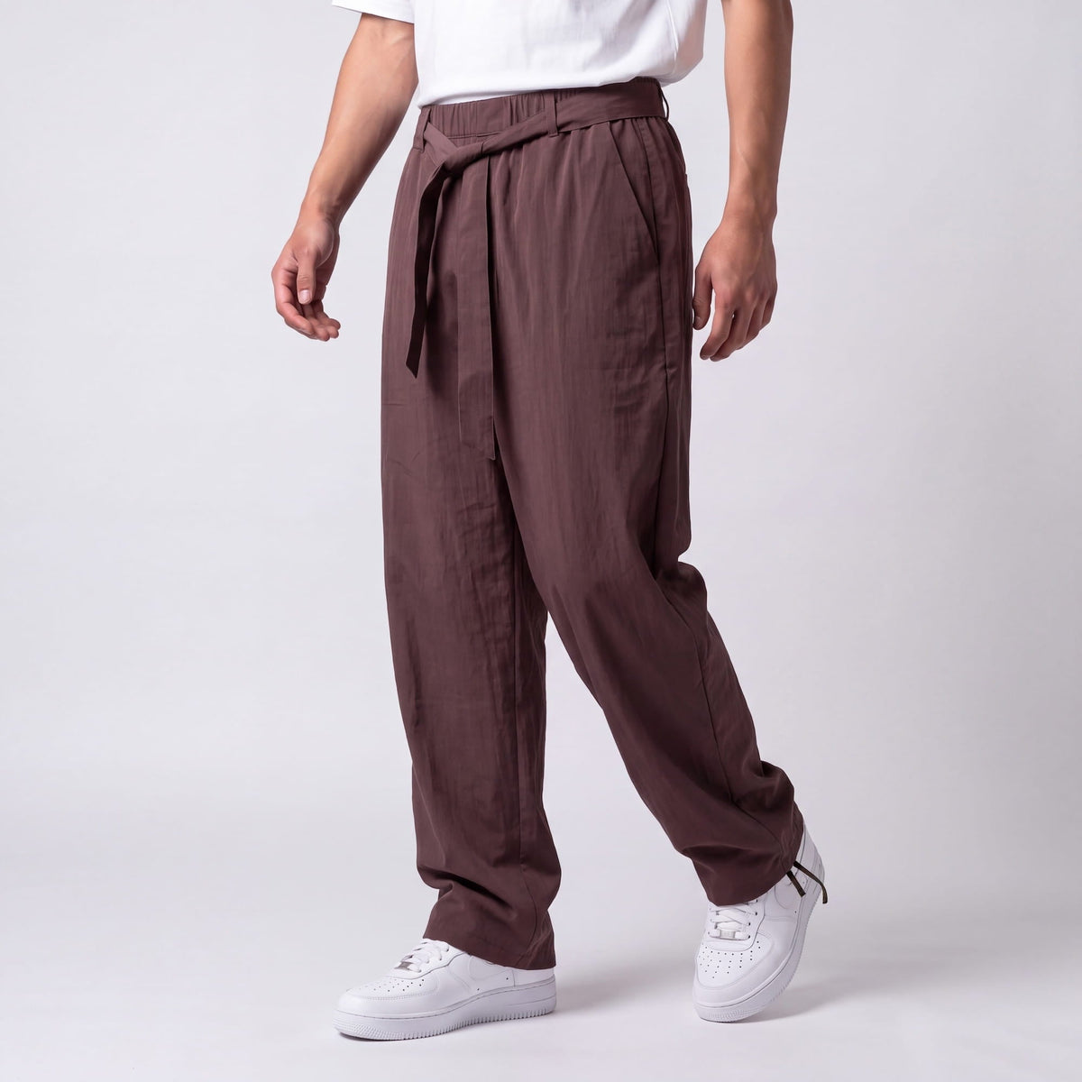 Angled three-quarter view of plum-brown trousers with tied belt and drawstring ankle, showing the loose, draped leg while walking. 8