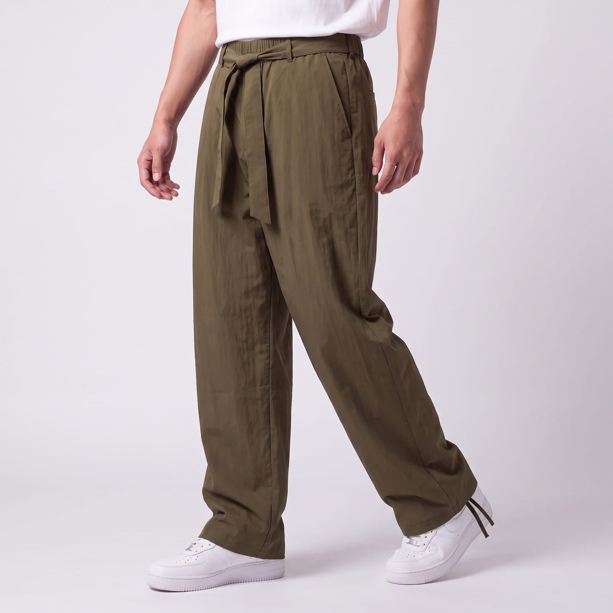 Angled view of olive green trousers with the belt tied at the front and drawstring ankles, worn with white trainers. 10