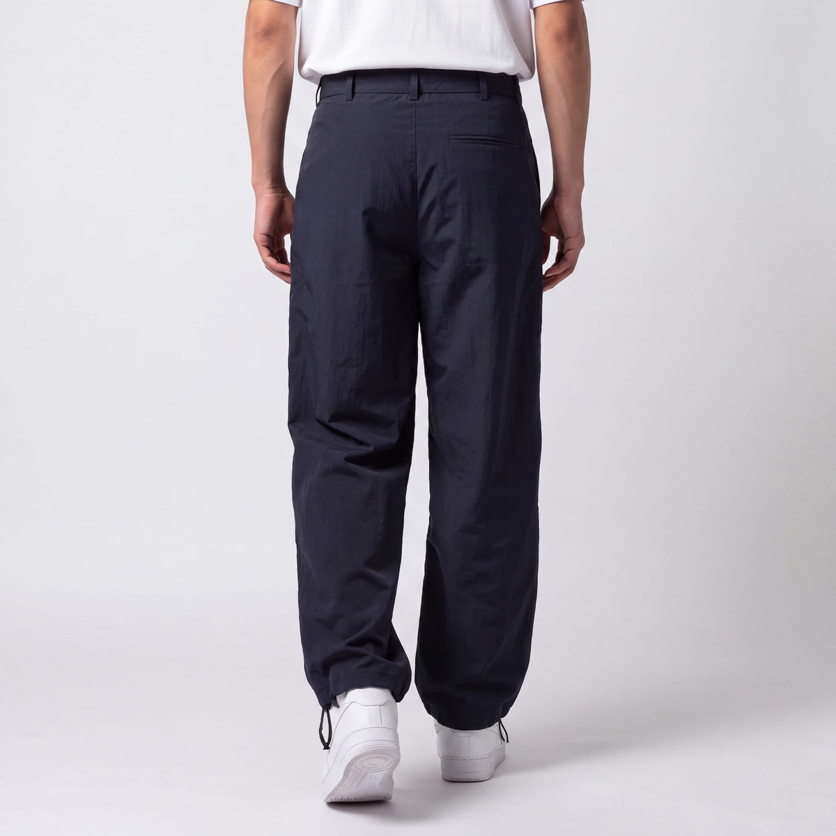 Back view of navy trousers on a model, showing the welt back pocket and drawstring ankle toggles above white trainers. 6