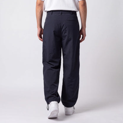 Back view of navy trousers on a model, showing the welt back pocket and drawstring ankle toggles above white trainers. 6