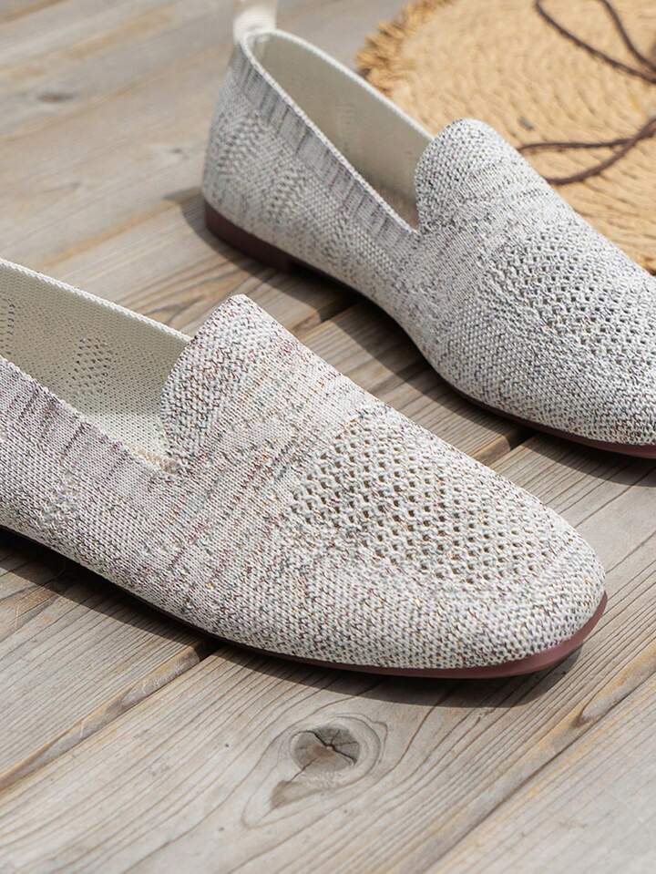 Close-up of light grey speckled knit slip-ons with a V-shaped opening and mesh toe panel on wooden decking. 16