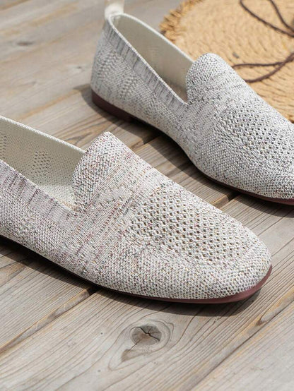 Close-up of light grey speckled knit slip-ons with a V-shaped opening and mesh toe panel on wooden decking. 16