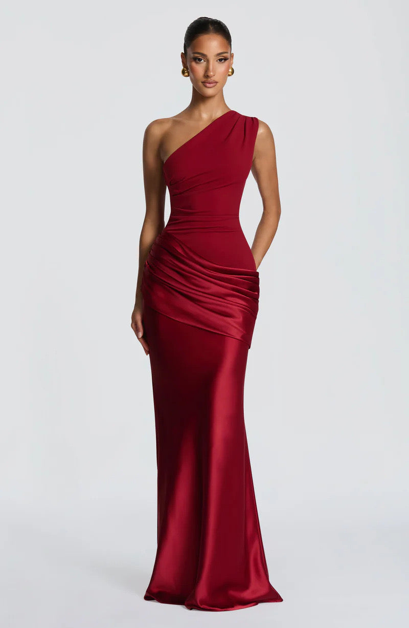 Front view of the deep red dress with one hand resting in a side pocket, showing the satin skirt and ruched waist. 24