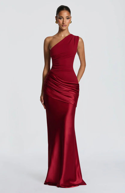 Front view of the deep red dress with one hand resting in a side pocket, showing the satin skirt and ruched waist. 24