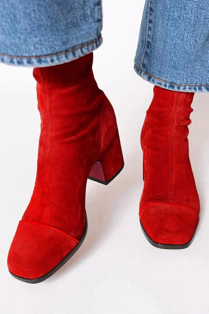 Red suede ankle boots with a flared block heel and stitched toe cap, worn with cropped blue jeans, seen from the front. 3