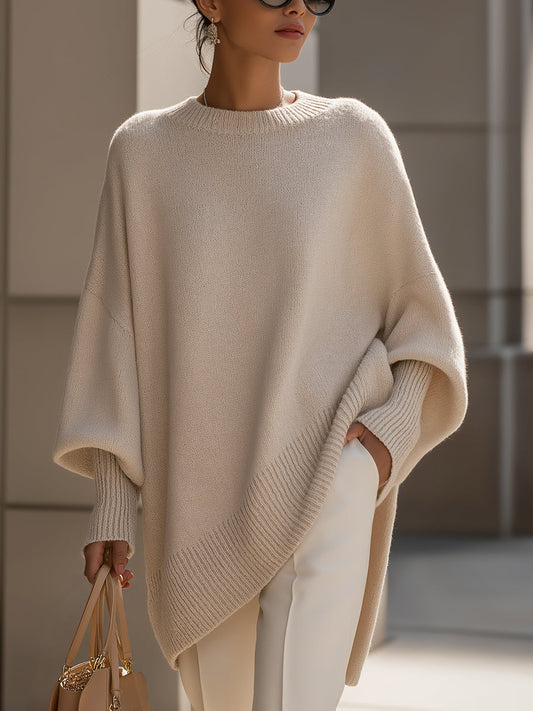 Beige knit poncho worn by a model against stone pillars, showing the wide batwing sleeves and ribbed hem 2
