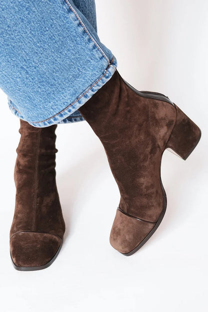 Dark brown suede ankle boots with a chunky heel and square toe cap, worn with turned-up blue jeans, seen from the side. 2