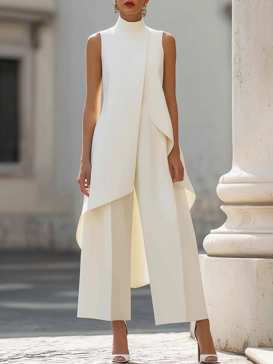 Cream version worn by a model, front view, with the asymmetric overlapping top draping over wide-leg trousers beside a stone column. 3