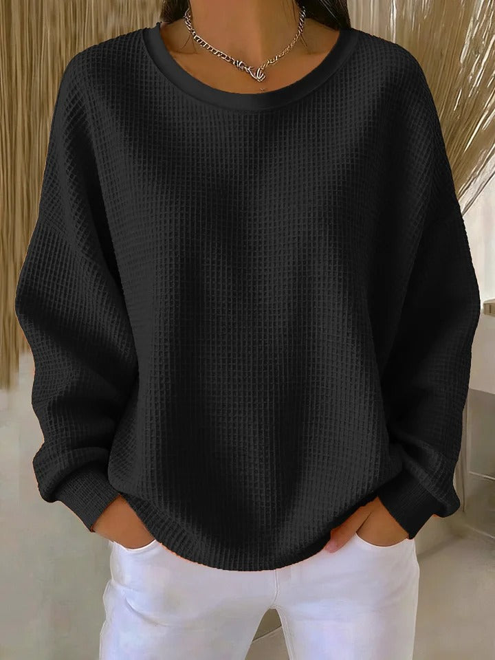 Model wearing the waffle-knit jumper in black, with a slouchy fit and ribbed cuffs, paired with white trousers. 7