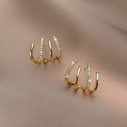 Pair of gold four-claw earrings on beige fabric, one showing its front, the other angled to the side 9