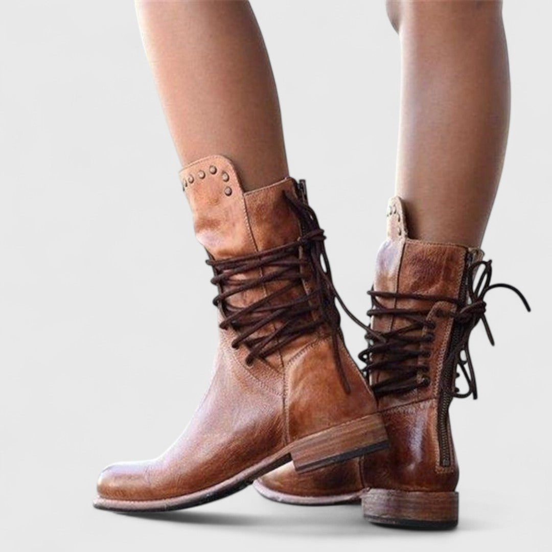 Rear view of brown leather boots on a model, showing the back zip, criss-cross laces and studded collars. 11