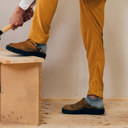 Person in mustard trousers and grey socks wearing the clogs, one foot raised on a wooden step 3