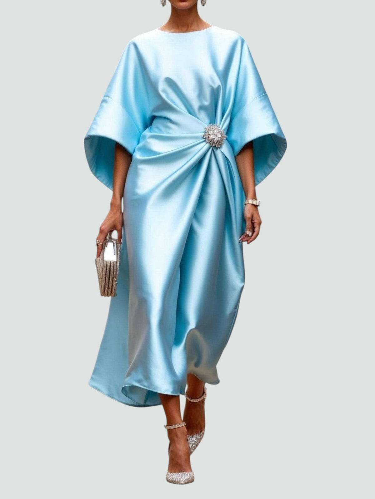 Model wearing the satin dress in pale sky blue, with wide cape sleeves, side draping and a crystal brooch at the waist. 3