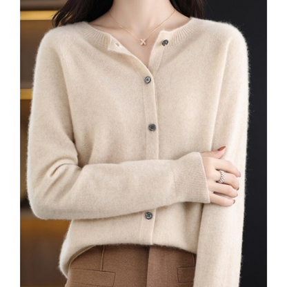 Pale cream cardigan on a model with arm folded across her body, showing the ribbed cuff, grey buttons and brown trousers. 15
