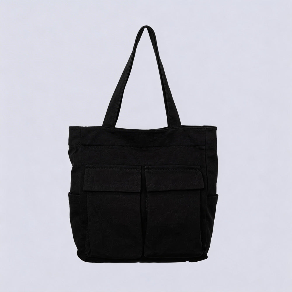 Black canvas tote bag seen from the front, with two large flap pockets, side pockets and two upright handles, against a plain pale background. 1