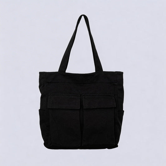 Black canvas tote bag seen from the front, with two large flap pockets, side pockets and two upright handles, against a plain pale background. 1