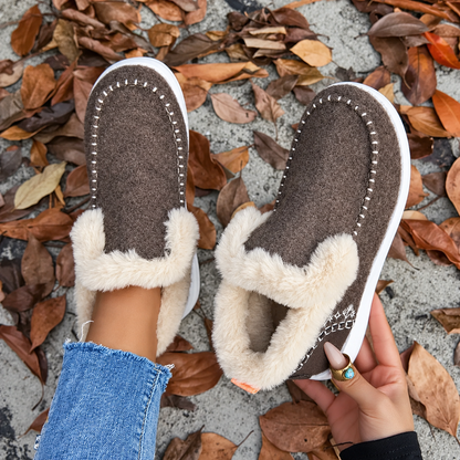 Overhead view of brown slip-ons, one on foot and one held to show the plush inner 8