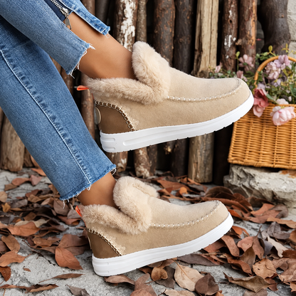 Beige suede-look slip-ons with fluffy collar and white sole, worn crossed-legged beside a wicker basket 3