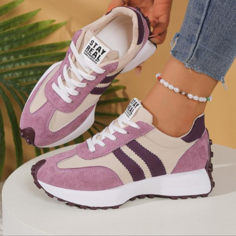 Lilac and beige trainers with dark purple stripes, worn with jeans in front of a palm leaf 11