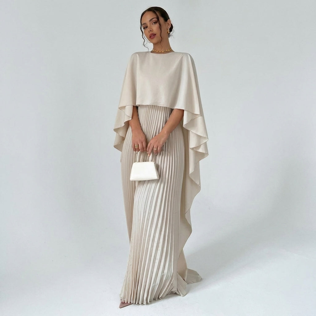 Model in the cream dress with draped cape top and pleated skirt, holding a small white handbag 1