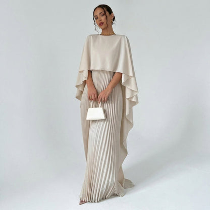 Model in the cream dress with draped cape top and pleated skirt, holding a small white handbag 1