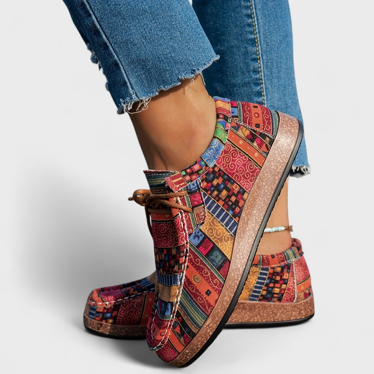 Rear side view of red, orange and blue geometric-print lace-up shoes with a thick cork-effect sole, worn with raw-hem jeans. 2