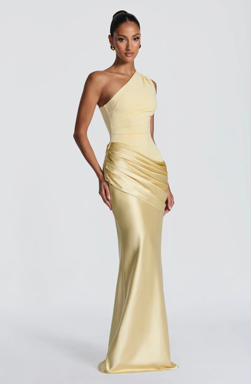 Angled view of the pale yellow one-shoulder dress, showing the pleated hip drape and glossy satin skirt falling to the floor. 26