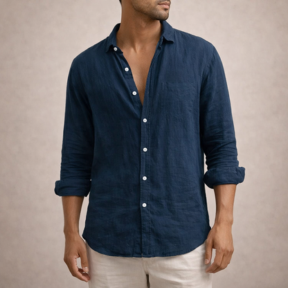 Navy linen shirt with a chest pocket and white buttons, worn by a model with rolled sleeves and light trousers. 7