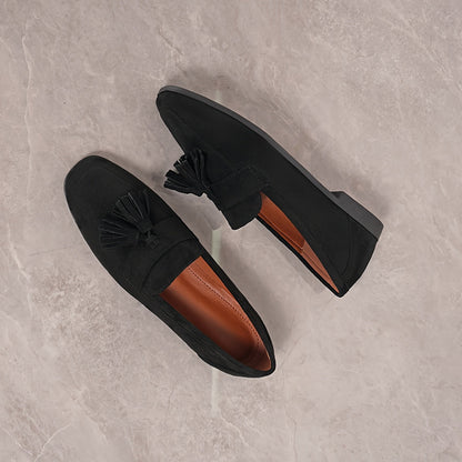 Overhead view of black tasselled loafers on marble, with tan lining visible inside 26