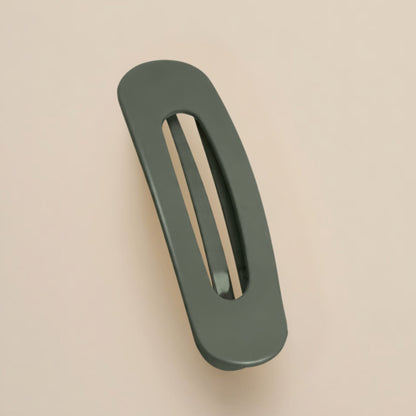 Matte dark olive green flat clip with a slim oval opening, shown from above on a peach-beige surface 16
