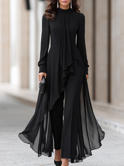 Model in a black chiffon tunic and wide-leg trousers, cropped from the chin down, holding a clutch 1