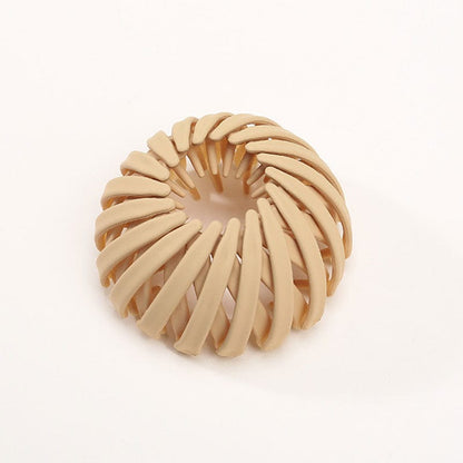 Single matte sand beige spiral bird's-nest clip on a plain pale background, showing its overlapping slats and open centre. 16