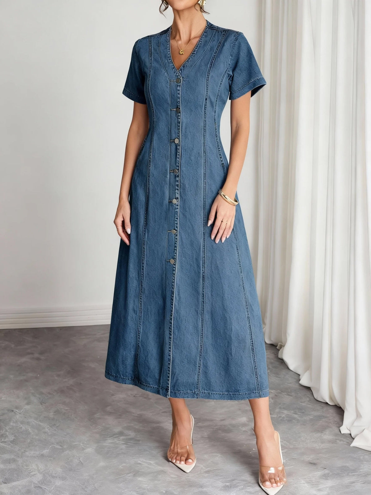 Three-quarter front view of the panelled denim dress, showing the metal button placket and flared skirt 4