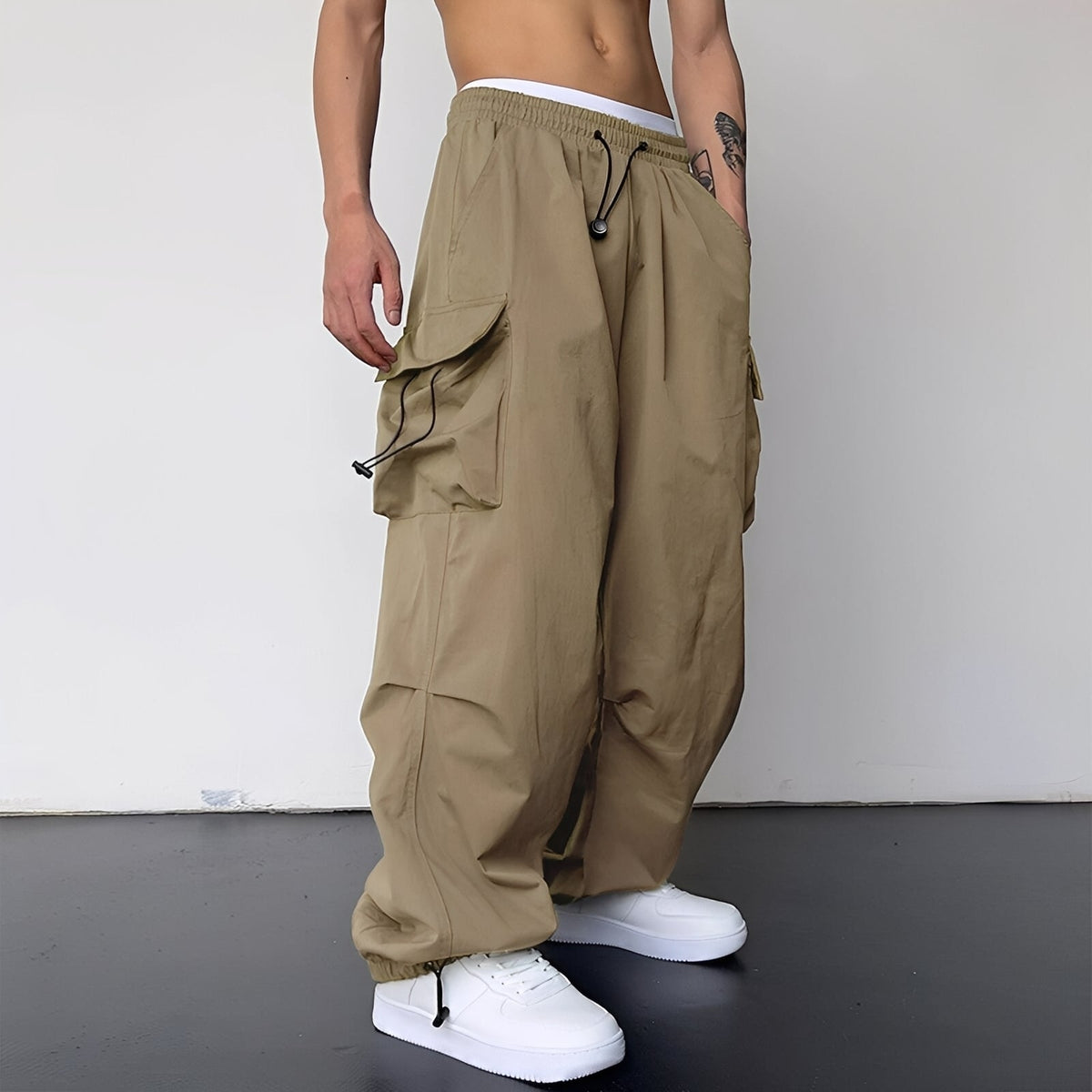 Model wears the baggy cargo trousers in sand beige with white trainers, side view 1