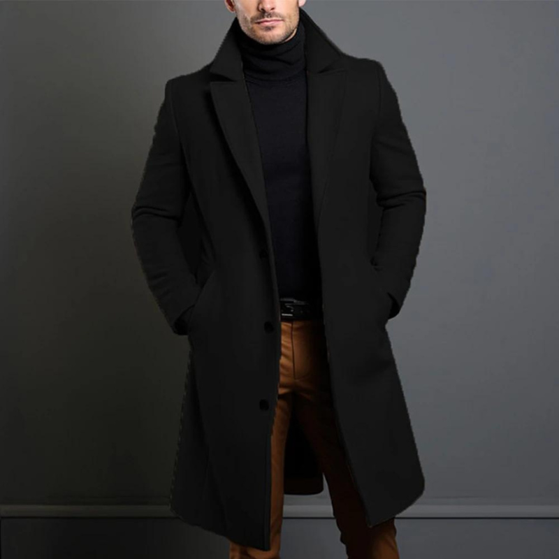 Model wearing the black single-breasted longline coat with notch lapels over a black roll-neck jumper and tan trousers, hands in pockets. 1