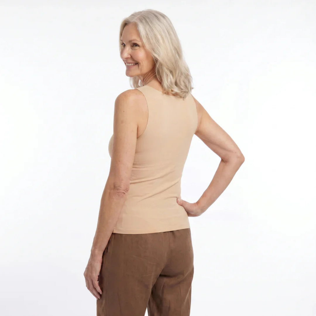 Back view of a smiling woman with silver hair wearing the sleeveless beige top with brown linen trousers, one hand on her hip. 6
