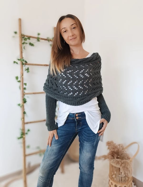 Dark grey lace-knit wrap with built-in sleeves, model standing front-on with one hand in a jeans pocket. 14