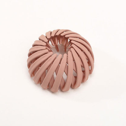 Single matte terracotta pink spiral bird's-nest clip on a plain pale background, with curved slats and inner prongs visible. 7