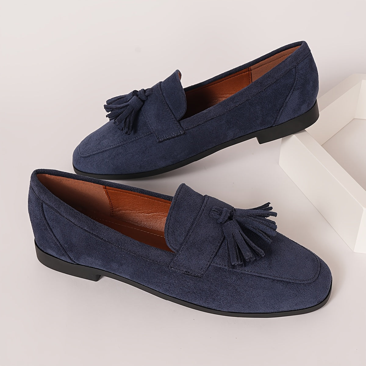 Pair of navy tasselled loafers with tan lining resting on a white block 6