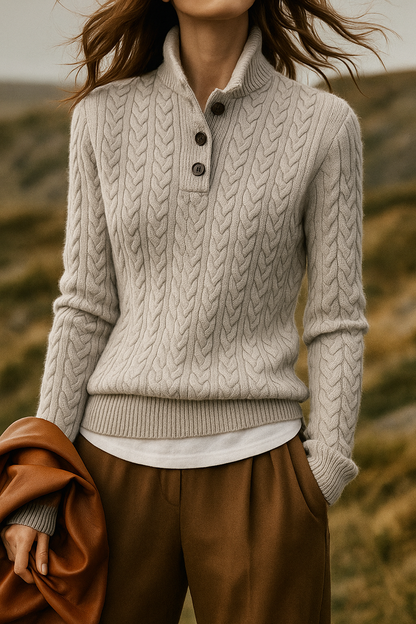 Model outdoors in the light grey cable-knit sweater with high buttoned collar, white top underneath, brown trousers and tan leather jacket. 13