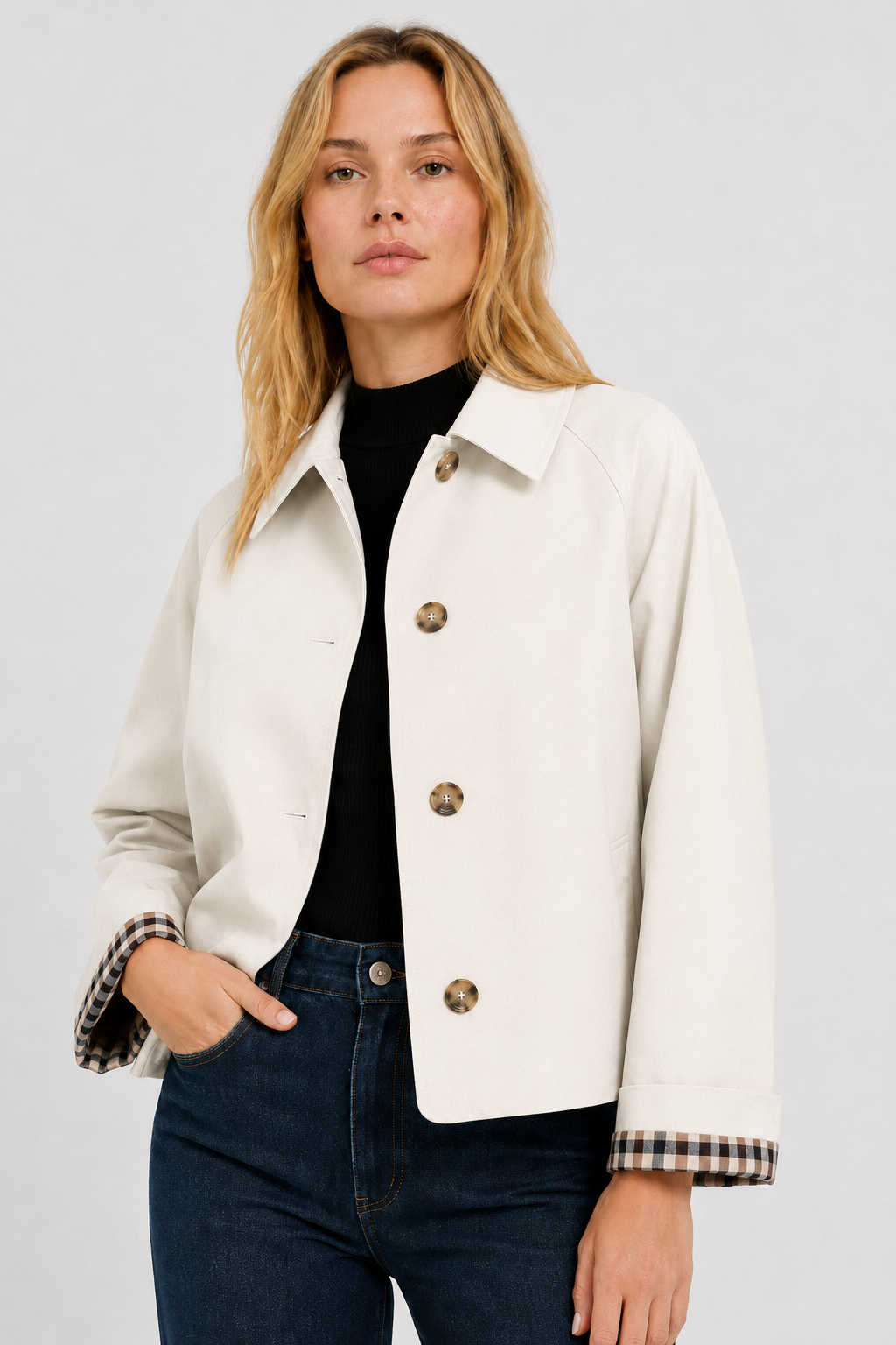 Model in a cream buttoned jacket over a black top and dark jeans, one hand in pocket, gingham cuff lining visible. 21