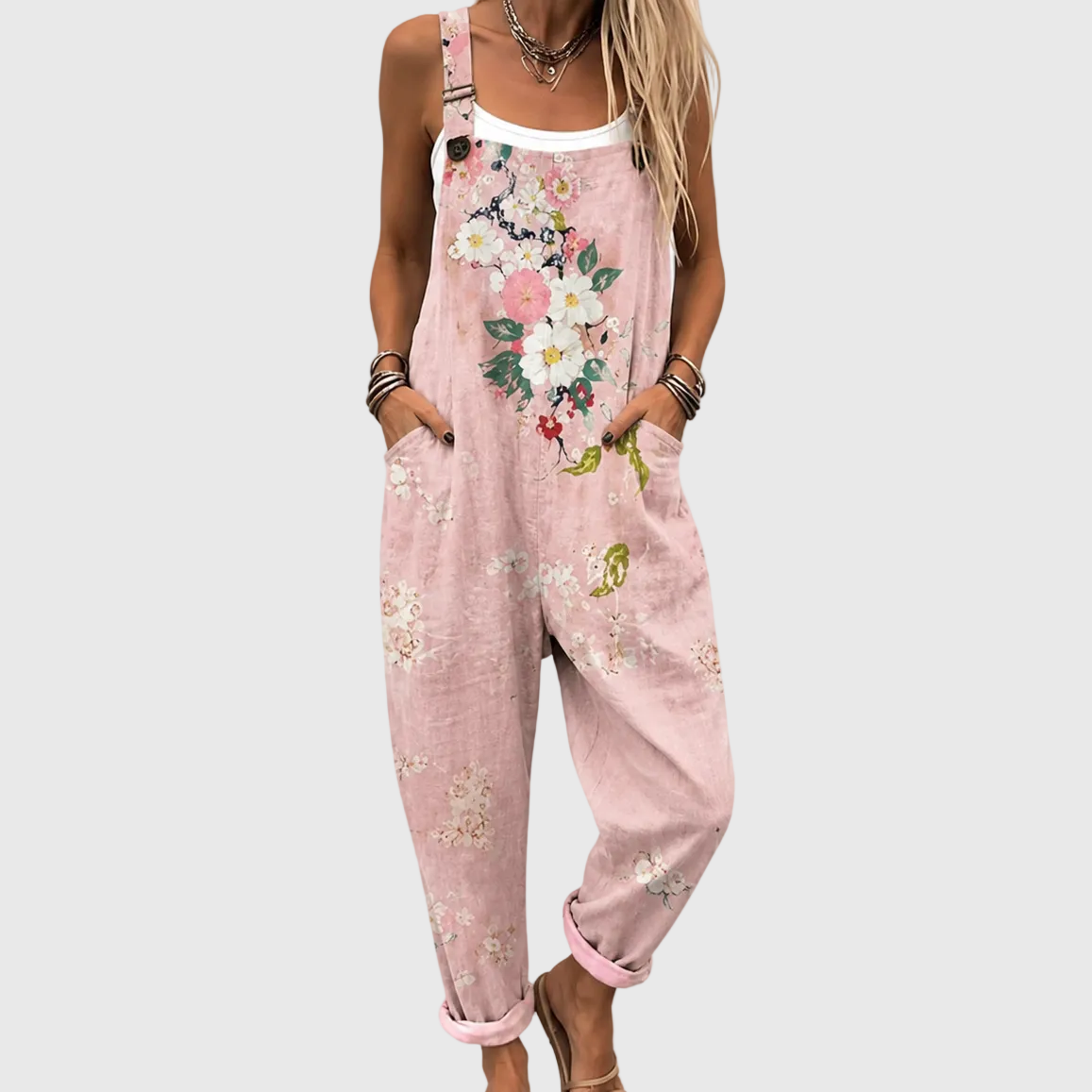 Close, cropped view of the floral overalls worn over a white vest, with hands in the side pockets and a button on the strap. 1