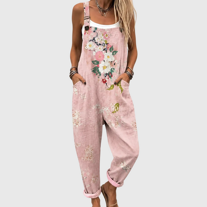 Close, cropped view of the floral overalls worn over a white vest, with hands in the side pockets and a button on the strap. 1