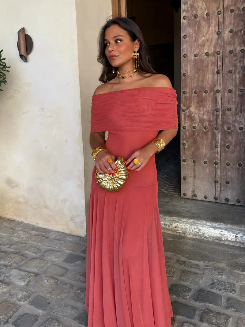 Front view of terracotta off-the-shoulder dress with a ruched neckline, holding a gold shell-shaped clutch 7