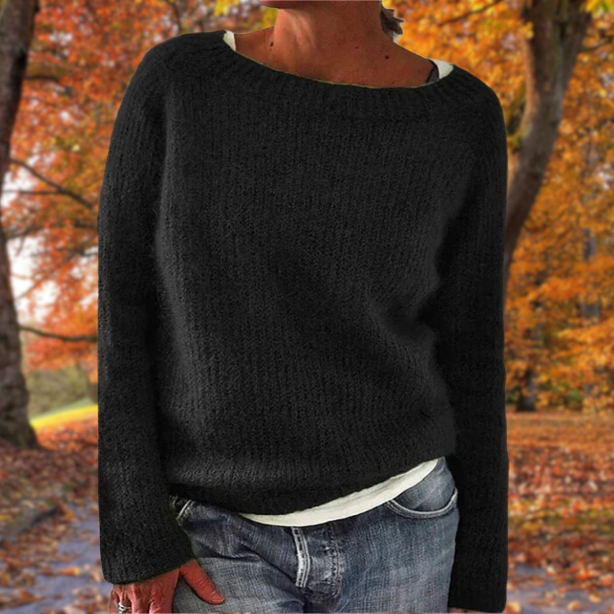 Black knit sweater with a wide neckline, worn by a model over a white top and jeans outdoors 2